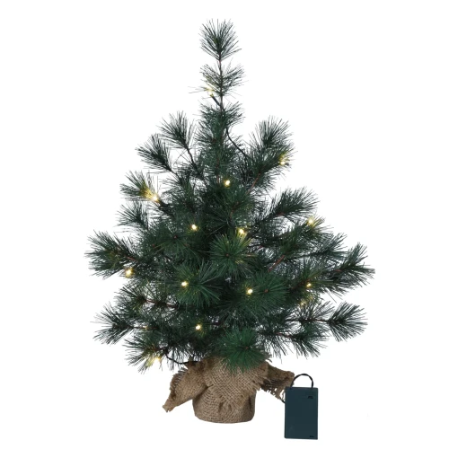 Sztuczna choinka z igliwiem PVC, ozdobiona ciepłymi lampkami LED, ustawiona w jutowym worku i zasilana bateriami przez zielony pojemnik.