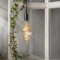 Żarówka LED dekoracyjna E27 w ryflowanym, wydłużonym kloszu zawieszona przy oknie z rośliną. Ciepłe światło tworzy przytulny klimat w jasnym, nowoczesnym wnętrzu.