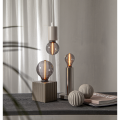 Trzy dekoracyjne żarówki LED z dymionym szkłem w lampach stołowych i wiszącej lampie w minimalistycznej aranżacji wnętrza na tle jasnych zasłon.