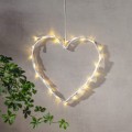 Wisząca dekoracja LED w kształcie serca emitująca ciepłe światło, umieszczona na jasnej ścianie obok zielonej rośliny.