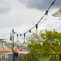 Girlanda świetlna z kloszami z tworzywa imitującego rattan, zamontowana na balkonie, widok na miasto w tle, dekoracyjne oświetlenie zewnętrzne.