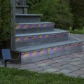 Wielokolorowa solarna taśma LED podświetlająca stopnie ogrodowych schodów. Na pierwszym planie widoczny panel solarny połączony z instalacją świetlną.