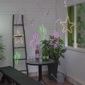 Girlanda świetlna z dekoracjami LED NEON: zielone kaktusy, różowe flamingi i żółte gwiazdy, zawieszone nad stołem w jasnym wnętrzu. Kolorowe oświetlenie dekoracyjne tworzy imprezowy klimat.