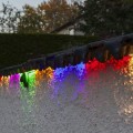 Wielokolorowy wąż LED zamontowany na krawędzi białego ogrodzenia, świecący w różnych barwach po zmroku.