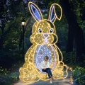 Wielkanocna iluminacja 3D LED w kształcie dużego zająca z siedziskiem, świetlna dekoracja miejska umożliwiająca robienie zdjęć, konstrukcja z ciepłobiałych diod LED ustawiona na placu miejskim.