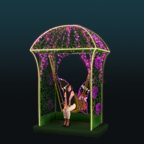 Podświetlana altana dekoracyjna z motywem roślinnym i motylem, pełniąca funkcję fotopunktu i strefy wypoczynkowej, z siedziskiem wewnątrz i osobą korzystającą z instalacji.