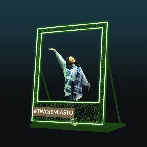 Dekoracyjna ramka LED w stylu polaroid na ciemnym tle z podświetlaną zieloną konstrukcją i miejscem na napis, nowoczesny fotopunkt do eventów, galerii handlowych i przestrzeni miejskich przyciągający uwagę.