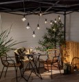 Girlanda ogrodowa LED zamontowana pod zadaszeniem tarasu, przezroczyste klosze w stylu retro emitujące ciepłe białe światło.