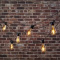Girlanda ogrodowa MIMOSA z żarówkami ST64 zawieszona przed ceglaną ścianą. Ciepłe światło LED 2000K, czarny przewód i dekoracyjny układ linii świetlnej.