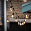 Girlanda świetlna BAJA z żarówkami LED E27 zawieszona nad przestrzenią zewnętrzną, ciepłe światło tworzące nastrojową atmosferę wieczorem.