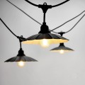 Zbliżenie na girlandę CRETE z czarnymi metalowymi kloszami i żarówkami LED E27. Widoczne ciepłe światło 2100K oraz modułowa konstrukcja przewodu z możliwością łączenia.
