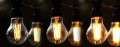 Girlanda ogrodowa z żarówkami LED A60 6,5W 2100K z 3-stopniowym ściemnianiem. Sześć żarówek w czarnych oprawkach, świecących na trzech poziomach jasności – od delikatnego po intensywne ciepłe światło. Tło rozmyte, ciemne.