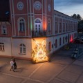 Wielkanocna dekoracja miejska LED w formie zająca z siedziskiem, instalacja świetlna ustawiona na rynku wśród zabudowy miejskiej i latarni.