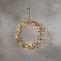 Złoty wianuszek dekoracyjny LED z listkami i drobnymi gwiazdkami, emitujący ciepłe światło, zawieszony na ścianie o naturalnej fakturze.