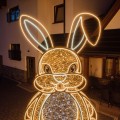 Duży zając wielkanocny LED z miejscem do siedzenia ustawiony przed wejściem do budynku, przestrzenna dekoracja świetlna z ażurową konstrukcją i świetlnym obrysem.