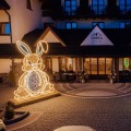 Wielkanocna iluminacja LED w kształcie zająca z siedziskiem ustawiona przed budynkiem hotelu, duża dekoracja świetlna do przestrzeni publicznych wykonana z ciepłobiałych diod LED.