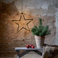 Wisząca gwiazda LED z drobnymi punktami świetlnymi zawieszona na łańcuchu; dekoracja ścienna na tle ceglanej ściany, obok donicy z zieloną rośliną i drewnianej ławki.