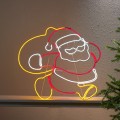 Dekoracja świetlna neon LED przedstawiająca Świętego Mikołaja, ustawiona przy ścianie. Czerwone, białe i żółte światło tworzy wyraźny kontur postaci i nadaje całości ciepły, świąteczny charakter.