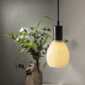 Żarówka LED Decoled Dream zawieszona na czarnym kablu, oświetlająca przestrzeń nad stołem z wazonem i roślinami w tle.