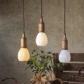 Trzy dekoracyjne lampy wiszące z drewnianymi oprawkami i ryflowanymi szklanymi kloszami w kształcie kropli emitujące różne barwy światła nad stołem z roślinami w naturalnej aranżacji wnętrza.
