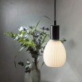 Żarówka LED Decoled Dream E27 w kolorze białym, zawieszona w oprawie nad stołem, z rozmytym tłem z roślinnością.