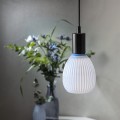 Żarówka LED Decoled Dream w kolorze błękitnym, zawieszona w nowoczesnej oprawie nad stołem. W tle rozmyta kompozycja z roślinami w wazonie.