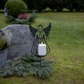 Dekoracja nagrobna anioł ze świecą LED wśród zieleni i kwiatów na cmentarzu.