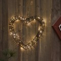 Dekoracja LED w kształcie serca ze sztucznego ratanu, z drobnymi ciepłymi diodami, zawieszona na ciemnej drewnianej ścianie.
