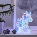 Geometryczna figurka jednorożca LED z transparentnego plastiku, świecąca wielokolorowym światłem, ustawiona na parapecie obok czarnych bombek i rośliny w białej doniczce, tworzy bajkową, świąteczną atmosferę.