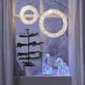 Jednorożec LED i choinka LED z transparentnego plastiku, ustawione na parapecie pod wiszącymi, świetlnymi wiankami w zimowej aranżacji wnętrza.