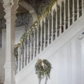 Zielona girlanda z rozłożystymi gałązkami i ciepłymi lampkami LED ułożona na balustradzie schodów w eleganckim, klasycznym wnętrzu.