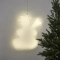 Bałwanek LED o ciepłym świetle, zawieszony na jasnej ścianie, tworzący miękki, świąteczny blask obok choinki.