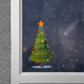 Naklejka LED przedstawiająca ozdobioną choinkę ze świecącą gwiazdą, przyklejona do szyby w białej ramie, z zimowym, rozmytym tłem za oknem.