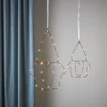 Dwie dekoracje LED w formie konturów Mikołajów, podświetlone ciepłym światłem, zawieszone na białych tasiemkach przed jasną ścianą i niebieską zasłoną.