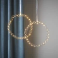 Dwa wianuszki LED w kolorze chromu o delikatnej, ażurowej formie plecionych okręgów z ciepłymi światełkami, zawieszone na subtelnych, dekoracyjnych taśmach.