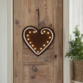 Wiszące piernikowe serce świąteczne LED z filcu, oświetlone ciepłymi diodami i zawieszone na drewnianych drzwiach.