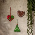 Trzy wiszące ozdoby LED w świątecznych kształtach — dwa serca i zielona choinka z podświetlanymi gwiazdkami — zawieszone na jasnej ścianie obok gałązek iglastych.