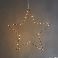 Delikatna gwiazda LED o ciepłej barwie światła, zawieszona na jasnej wstążce i miękko rozświetlająca szarą ścianę. Subtelna, przytulna dekoracja do wnętrz.