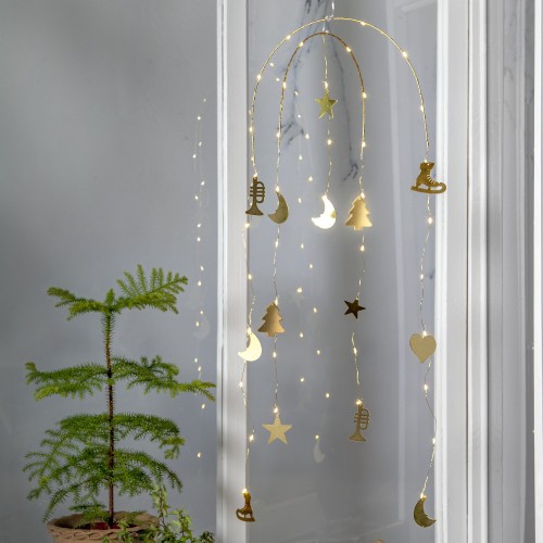 Delikatna dekoracja LED z lekkimi, złotymi zawieszkami układającymi się w świąteczne motywy, subtelnie rozświetla przestrzeń przy oknie ciepłym światłem, wprowadzając do wnętrza spokojny, przytulny nastrój.