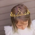 Dziecko w mosiężnej koronie LED, której ciepły blask podkreśla subtelność świątecznego stroju.