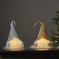 Złoty i srebrny skrzat LED z brokatowymi czapkami i subtelnym podświetleniem brody, stojące obok siebie na stole przy udekorowanej choince.