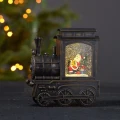 Podświetlana świąteczna lokomotywa wodna LED w kolorze postarzanego brązu, z figurką Mikołaja, choinką i prezentami w wirującym brokacie, ustawiona na ciemnym blacie na tle choinki z ciepłymi lampkami.
