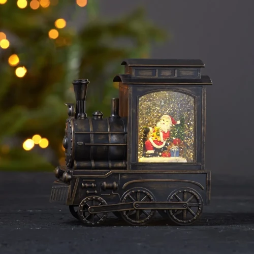 Podświetlana świąteczna lokomotywa wodna LED w kolorze postarzanego brązu, z figurką Mikołaja, choinką i prezentami w wirującym brokacie, ustawiona na ciemnym blacie na tle choinki z ciepłymi lampkami.