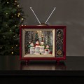 Podświetlany świąteczny telewizor retro LED w czerwonej obudowie, w środku scena z rodziną bałwanków na tle choinek w wirującym brokacie, ustawiony na ciemnym blacie przy choince z lampkami.
