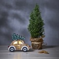 Podświetlana dekoracja drewniane auto z choinką i napisem MERRY X-MAS, emitujące ciepłe światło LED, ustawione obok małego drzewka w donicy, tworząca nastrojowy, zimowy klimat na świątecznym stole.