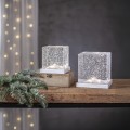 Dwie dekoracyjne kostki LED z przezroczystymi ściankami i połyskującymi drobinkami, ustawione na drewnianej półce.