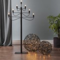 Dwie czarne kule LED z metalowego drutu ustawione na podłodze obok wysokiego świecznika i rośliny doniczkowej. Ciepłe światło w ażurowych splotach tworzy spokojną, dekoracyjną kompozycję we wnętrzu.