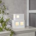 Lampa dekoracyjna dom LED w białej obudowie z widocznymi, podświetlanymi oknami, pokazana w prostej aranżacji z rośliną. Miękkie, ciepłe światło podkreśla przytulny charakter dekoracji.