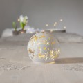 Dekoracja stołowa LED w formie białej kuli z ciepłym światłem, złote motywy jeleni, choinek i napis „Merry Christmas”, ustawiona na jasnym blacie; nastrojowa, świąteczna atmosfera.