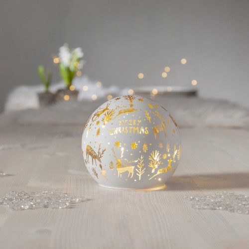 Dekoracja stołowa LED w formie białej kuli z ciepłym światłem, złote motywy jeleni, choinek i napis „Merry Christmas”, ustawiona na jasnym blacie; nastrojowa, świąteczna atmosfera.